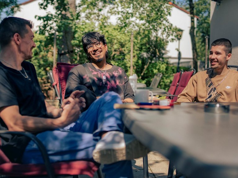 Drei  junge Männer sitzen in der Sonne um einen Tisch herum