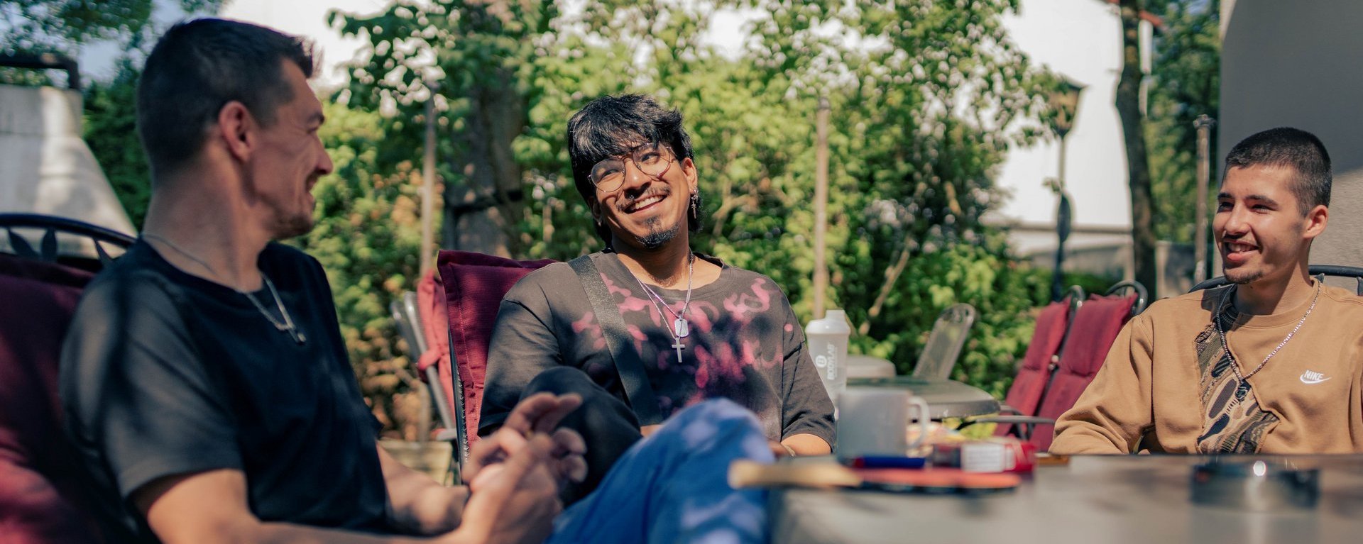 Drei junge Männer sitzen in der Sonne und unterhalten sich im Adaptionshaus Kieferngarten