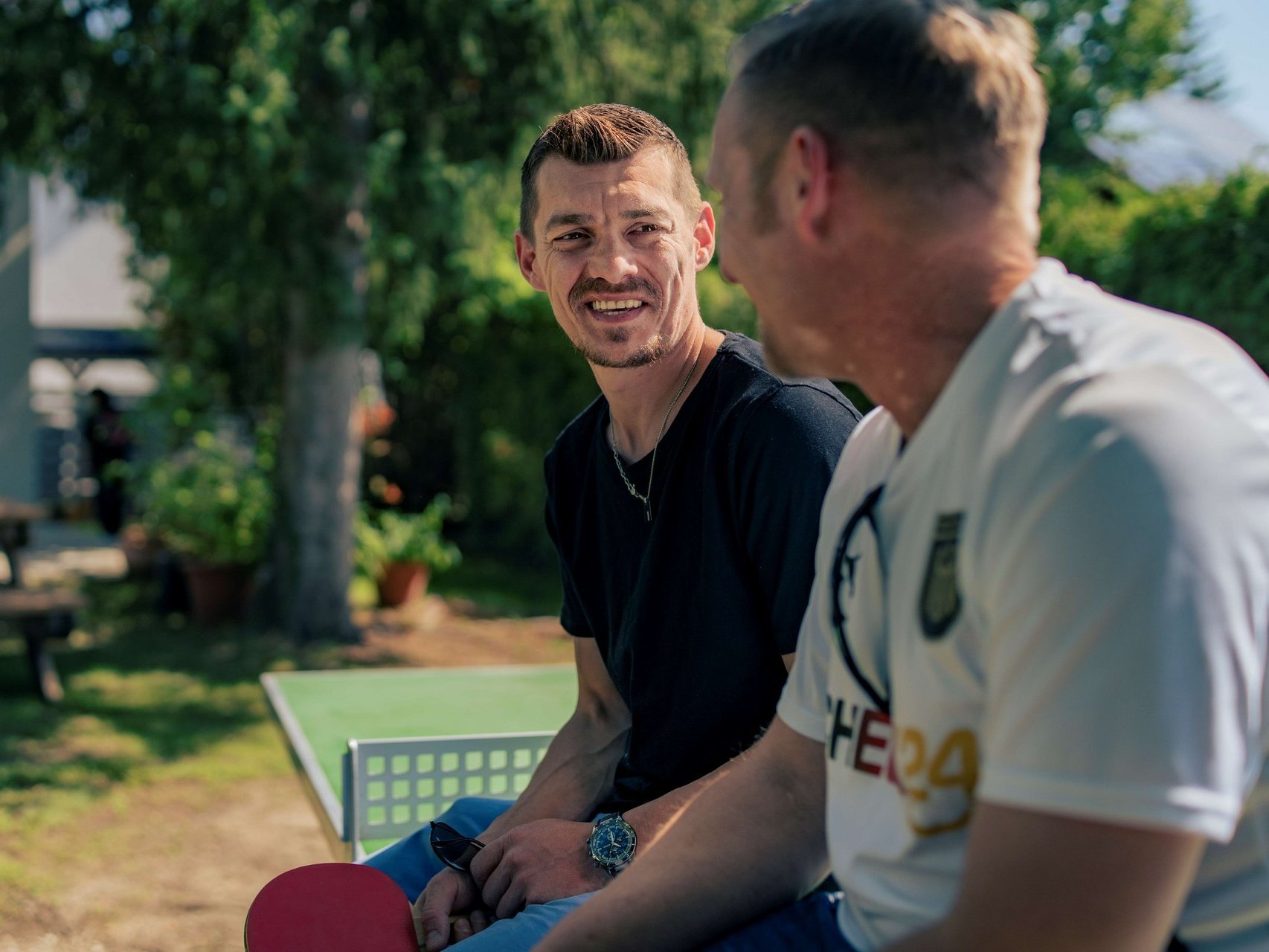 Zwei junge Maenner sitzen auf einer Tischtennisplatte und unterhalten sich