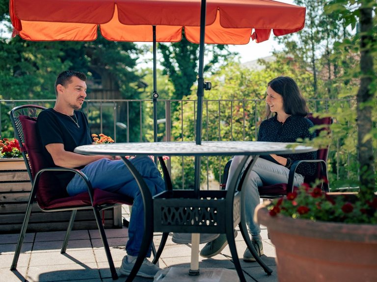 Eine Therapeutin und ein Mensch mit Suchterkrankung unterhalten sich auf einer Terrasse